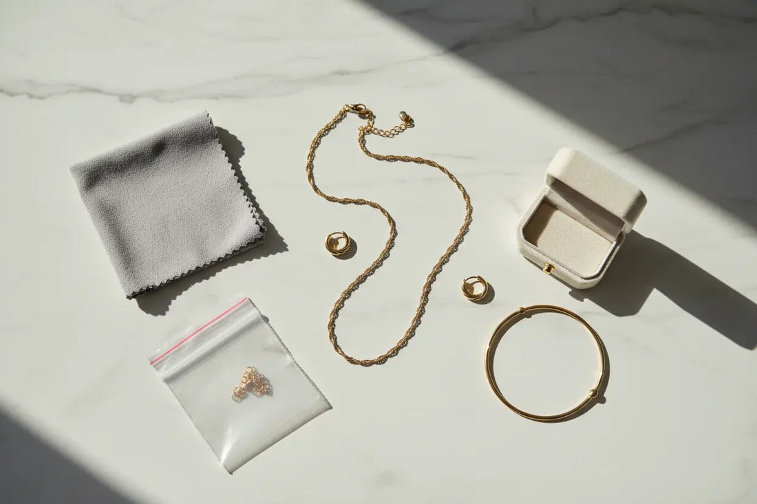 Flat lay of fashion jewellery care essentials — polishing cloth, storage pouch and gold jewellery pieces on marble background