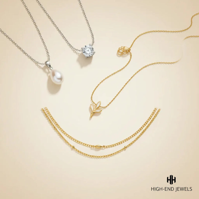 Four delicate jewelry pieces arranged on a warm cream background: a silver chain necklace with a white pearl pendant, a silver small leaf pendant, and a double-layered gold chain necklace.