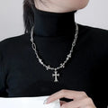 Person wearing a black turtleneck with a silver necklace featuring a cross pendant.