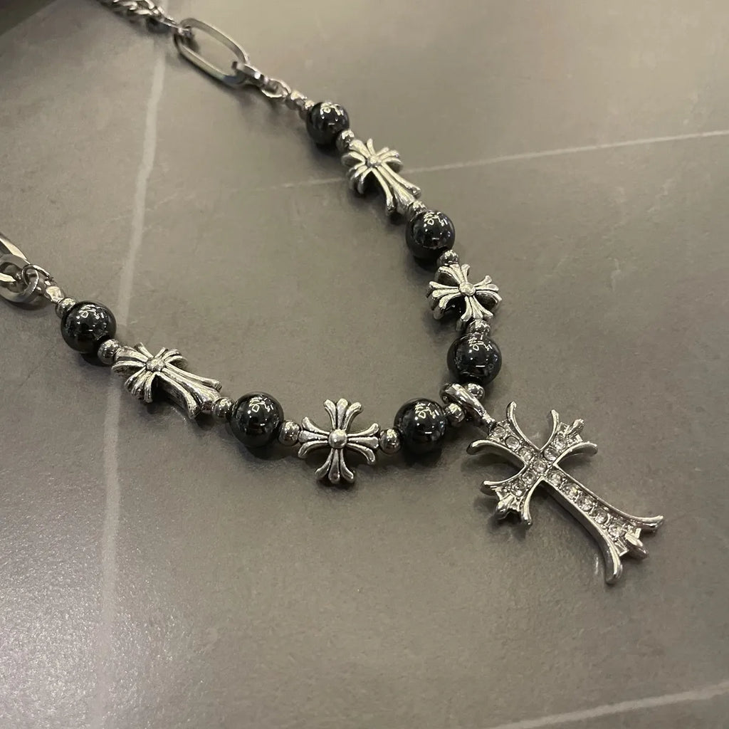 Necklace with black beads and silver crosses on a reflective surface