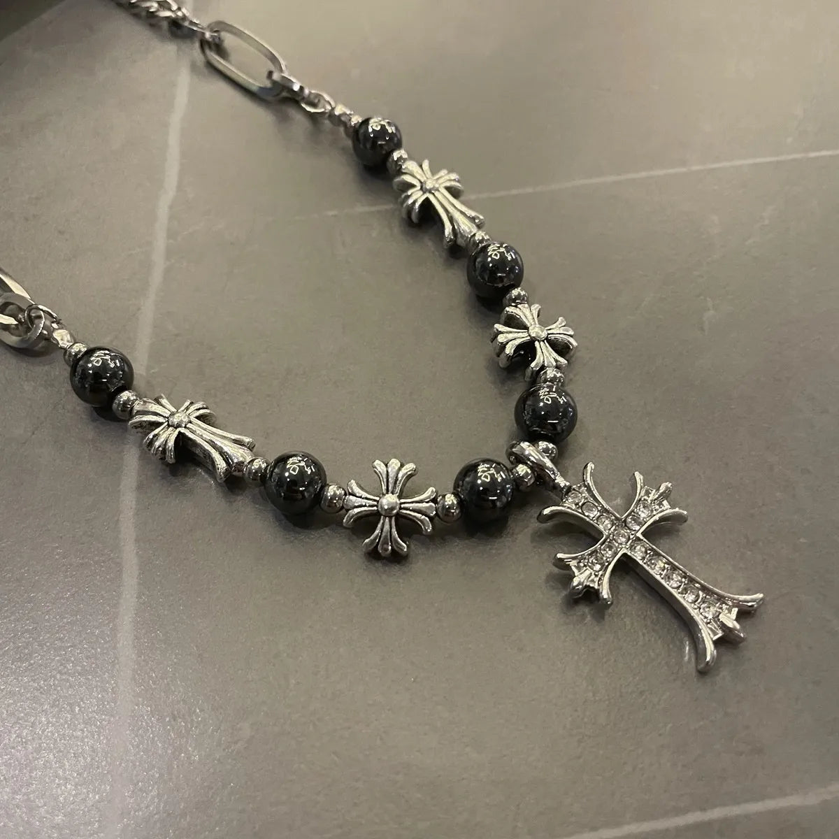Necklace with black beads and silver crosses on a reflective surface