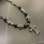 Necklace with black beads and silver crosses on a reflective surface