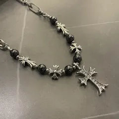 Necklace with black beads and silver crosses on a reflective surface