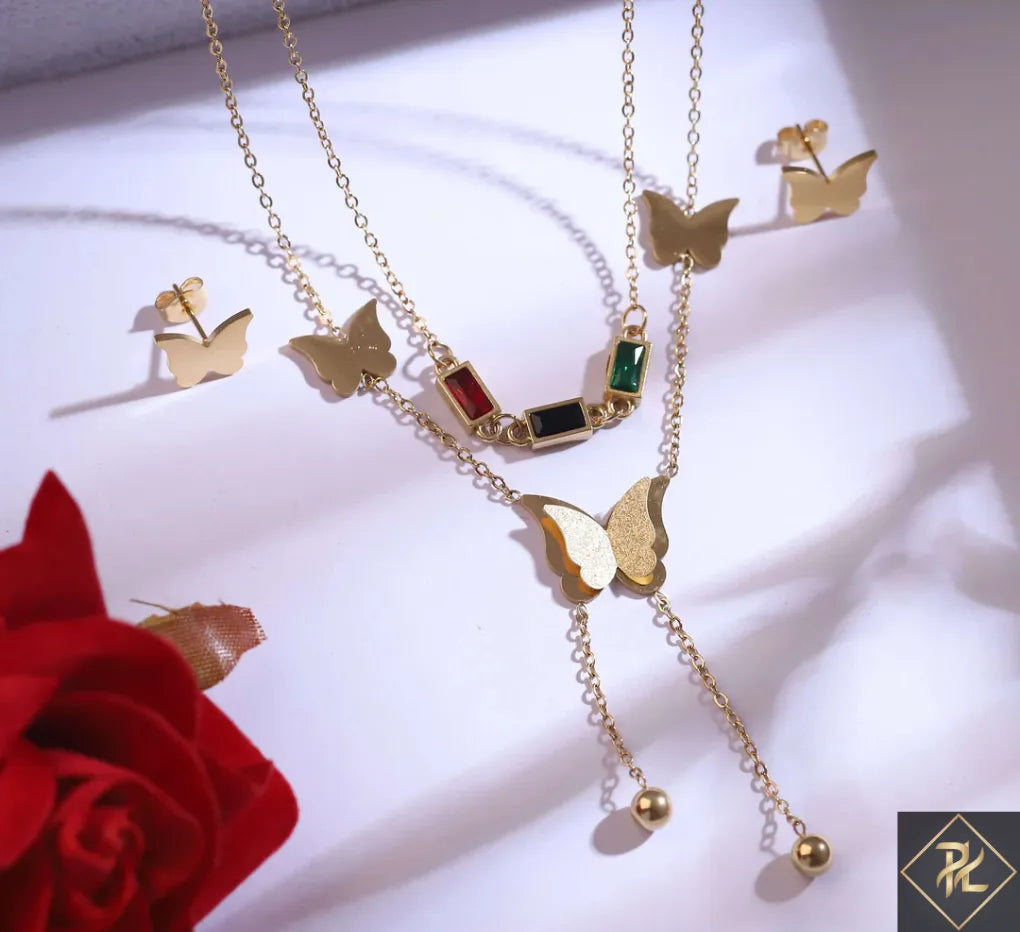 Gold butterfly necklace with gemstones on a white surface with a red rose.