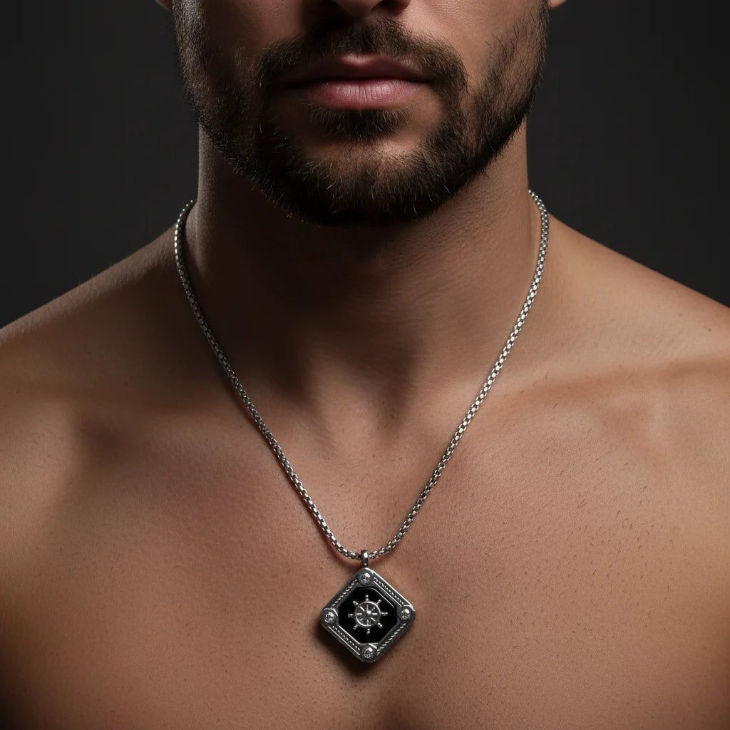 A close-up of a man's neck and chest wearing a silver chain necklace with a diamond-shaped pendant featuring a black center and a silver compass-like design.