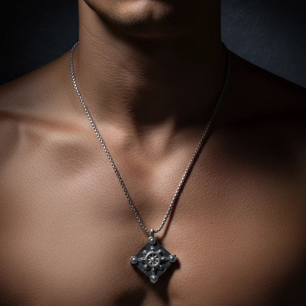 A close-up of a man's neck and chest wearing a silver chain necklace with a diamond-shaped pendant featuring a central floral or snowflake-like motif and small clear stones at the corners.