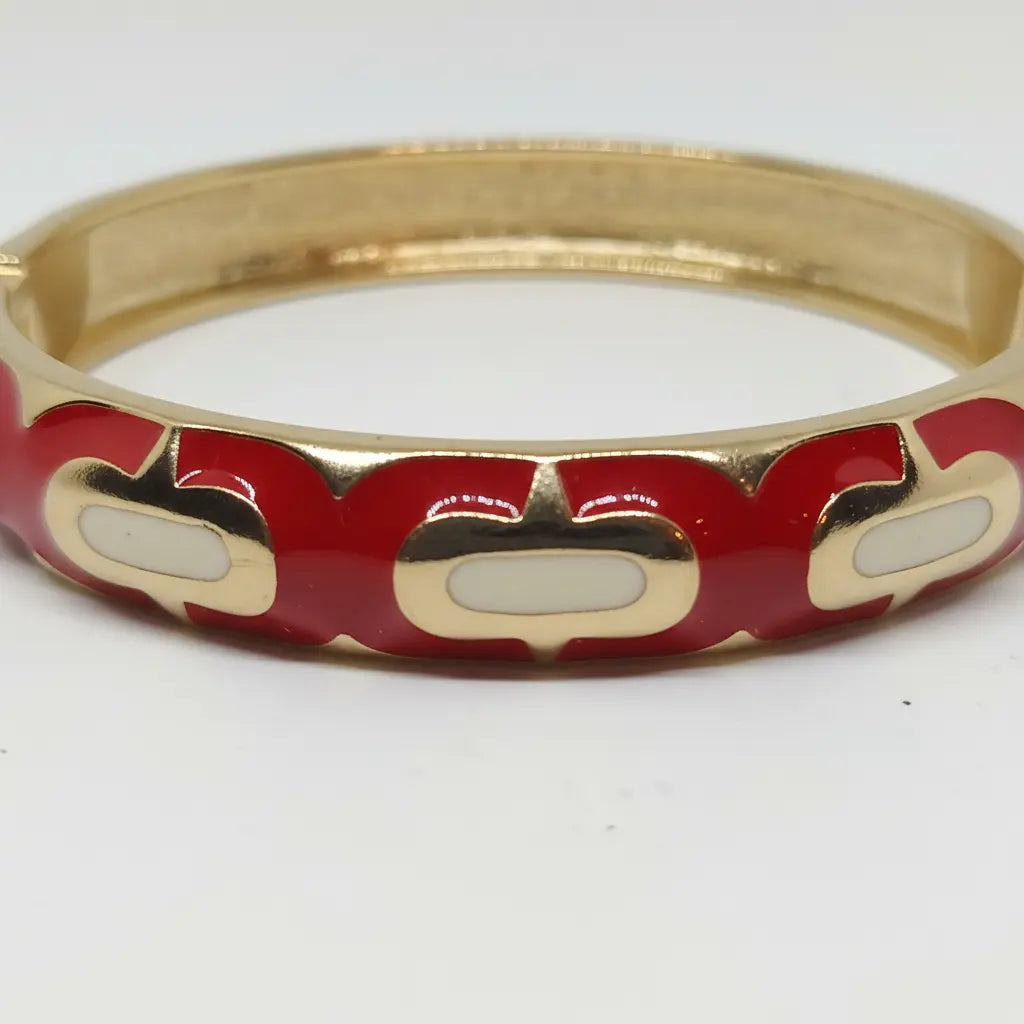 A gold-plated bangle bracelet featuring a red enamel inlay with white oval accents, shown on a plain white background.