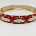 A gold-plated bangle bracelet featuring a red enamel inlay with white oval accents, shown on a plain white background.