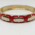 A gold-plated bangle bracelet featuring a red enamel inlay with white oval accents, shown on a plain white background.
