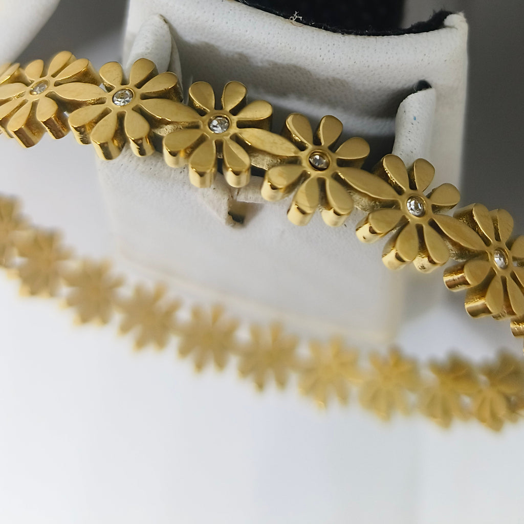 A gold-tone floral bangle bracelet with small clear rhinestone centers, displayed on a white jewelry stand.