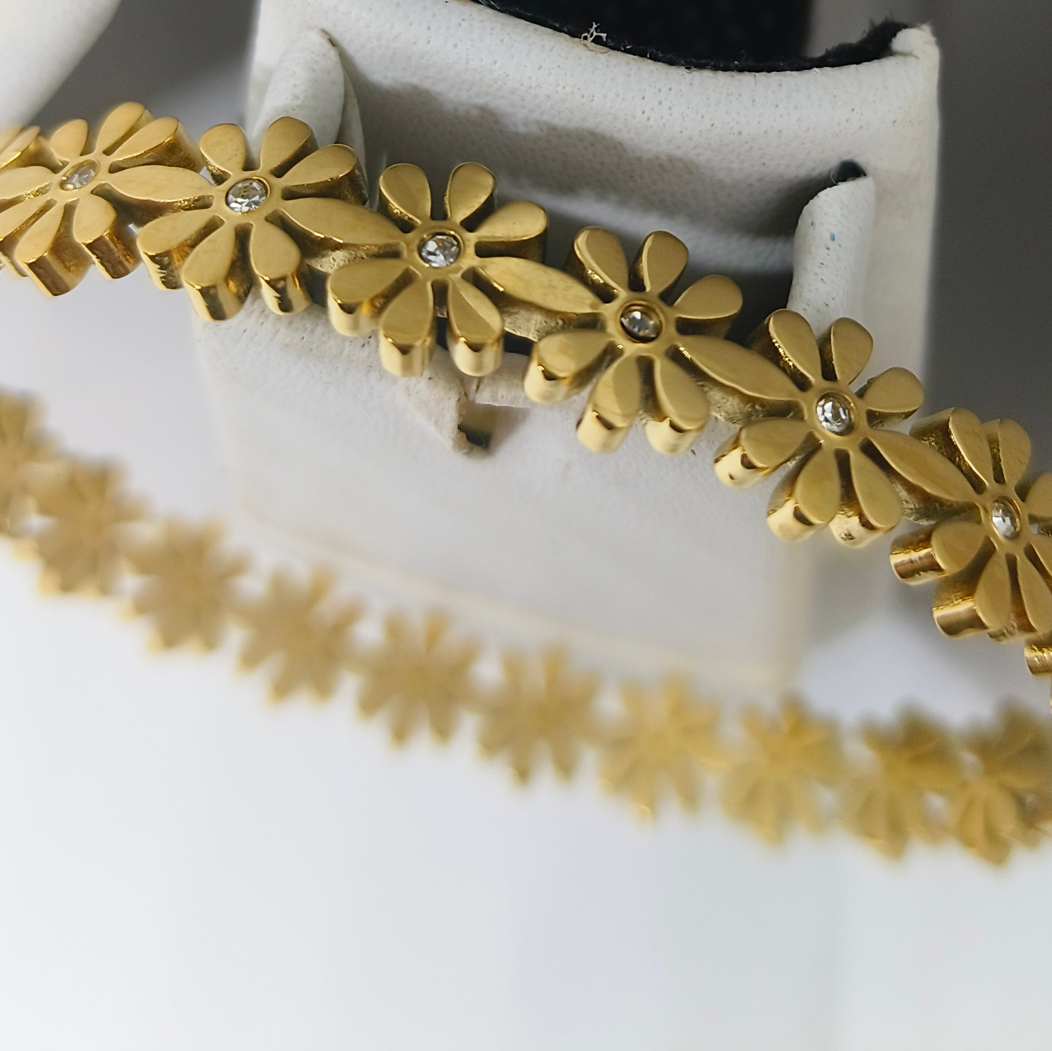 A gold-tone floral bangle bracelet with small clear rhinestone centers, displayed on a white jewelry stand.