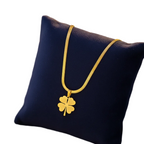 A gold chain necklace with a four-leaf clover pendant displayed on a dark blue velvet cushion.