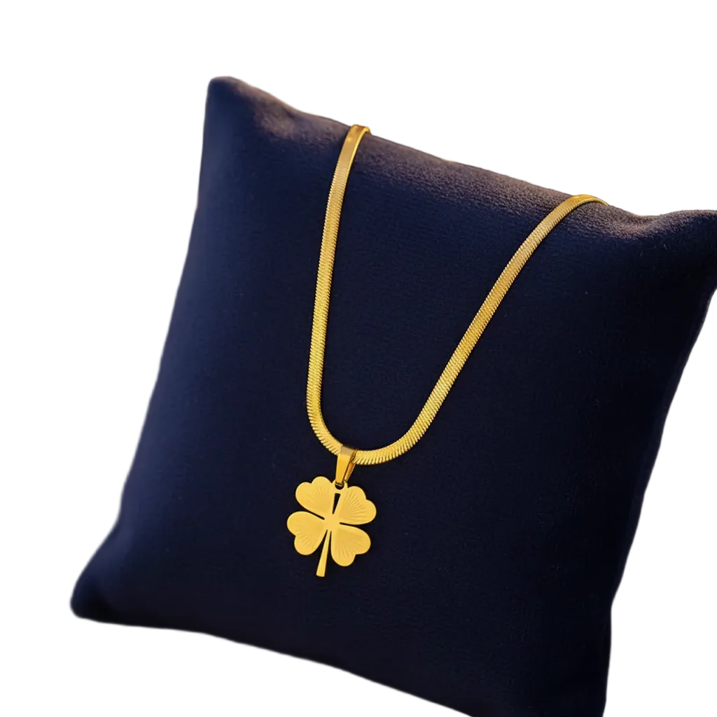 A gold chain necklace with a four-leaf clover pendant displayed on a dark blue velvet cushion.