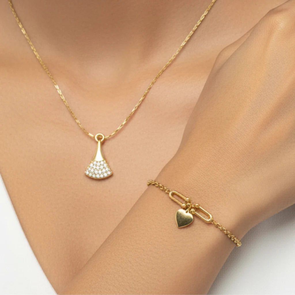 A gold necklace and matching bracelet displayed on a model's neck and wrist. The necklace features a delicate gold chain with a pendant shaped like a small fan or shield, adorned with clear pavé stones.