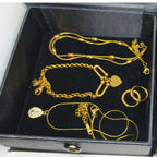A set of gold jewelry pieces, including a chain necklace, bracelet, rings, and pendant, displayed inside a black presentation box.