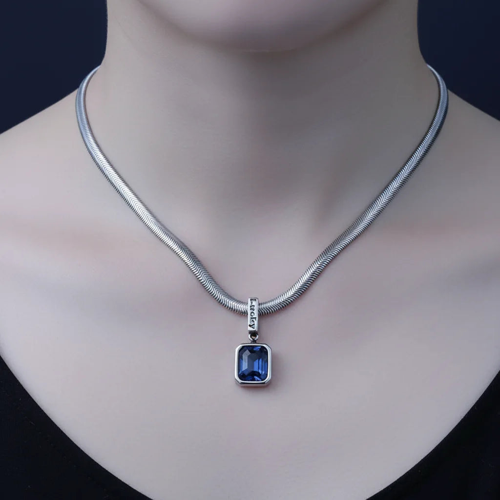 A silver snake chain necklace with a rectangular blue gemstone pendant, displayed on a mannequin neck against a dark background.
