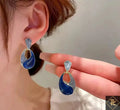 Blue and silver earrings being held up to a person's ear.
