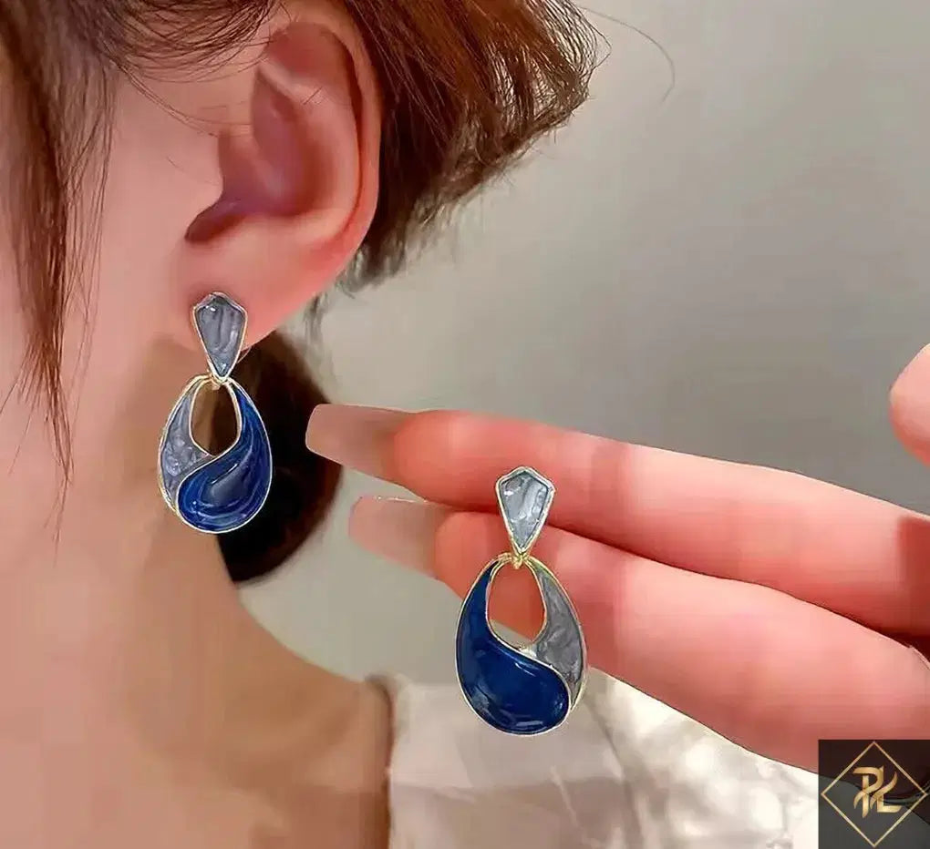 Blue and silver earrings being held up to a person's ear.