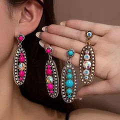 Earrings with colorful gemstones worn by a person, held up to the ear.
