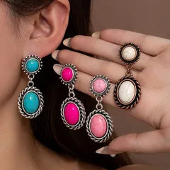 Colorful earrings being worn and held by a hand against a neutral background