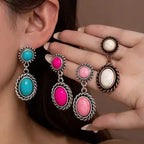 Colorful earrings being worn and held by a hand against a neutral background