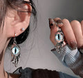 Close-up of a person wearing silver earrings with eye design, holding one earring.