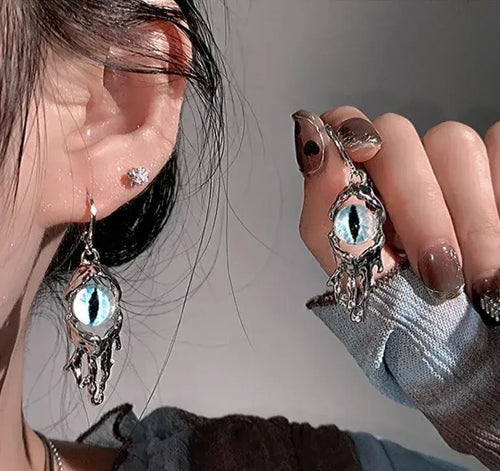 Close-up of a person wearing silver earrings with eye design, holding one earring.