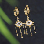 Gold hoop earrings with dangling floral designs on a dark background