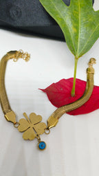 Evil's Eye Leaf Charm Snake Chain Bracelet featuring a gold-plated four-leaf clover charm with a small blue evil eye pendant on a sleek snake chain, styled with green and red leaves.