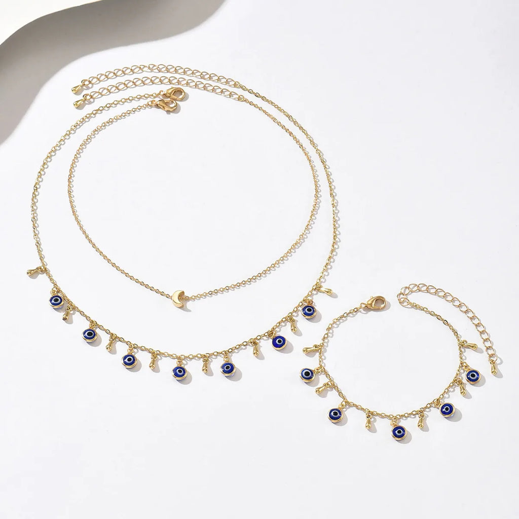 Gold necklace and bracelet set with blue eye charms on a white background