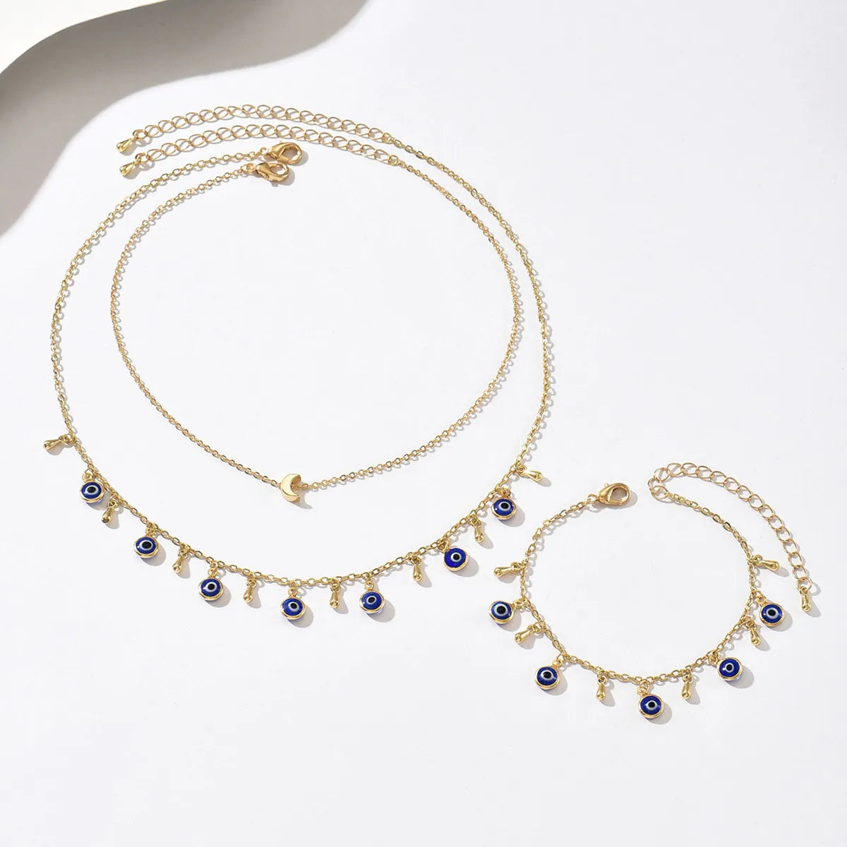 Gold necklace and bracelet set with blue eye charms on a white background
