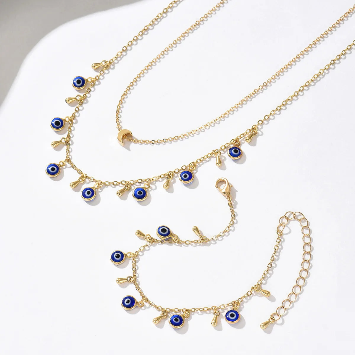Gold necklaces with blue evil eye charms on a white surface