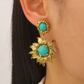 Gold earrings with turquoise stones worn by a person