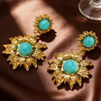 Gold earrings with turquoise stones on a brown fabric background