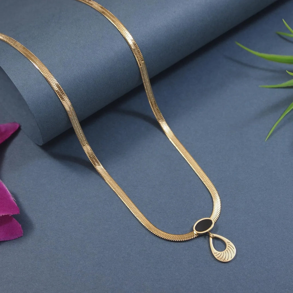 Gold necklace with a teardrop pendant on a blue surface