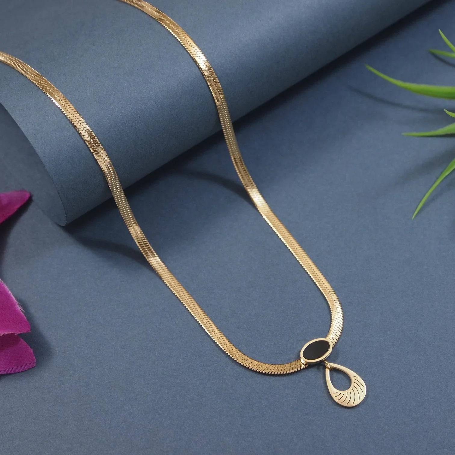 Gold necklace with a teardrop pendant on a blue surface