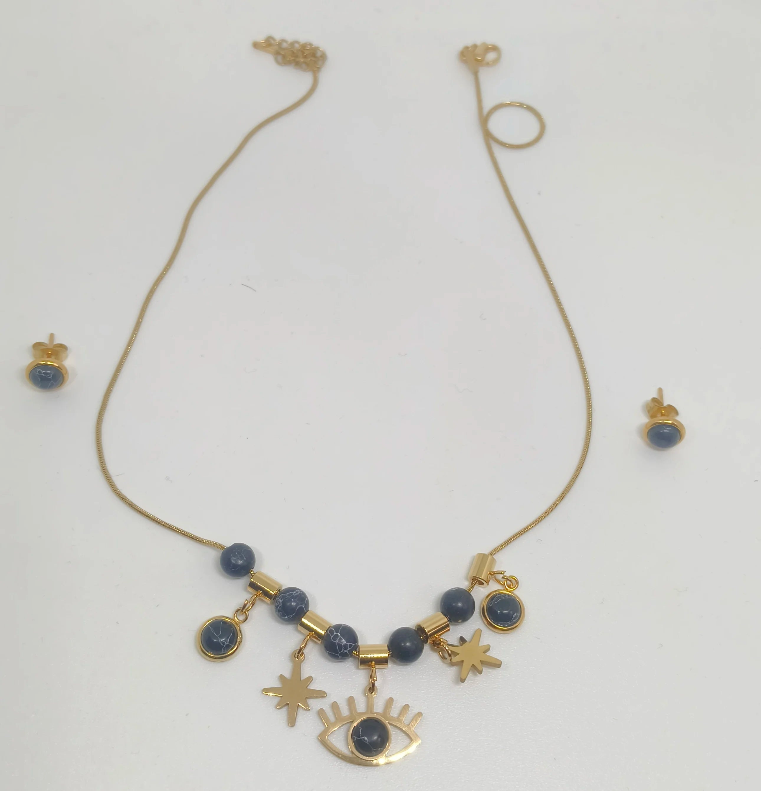 Gold necklace with blue beads and star, eye, and moon charms on a white background