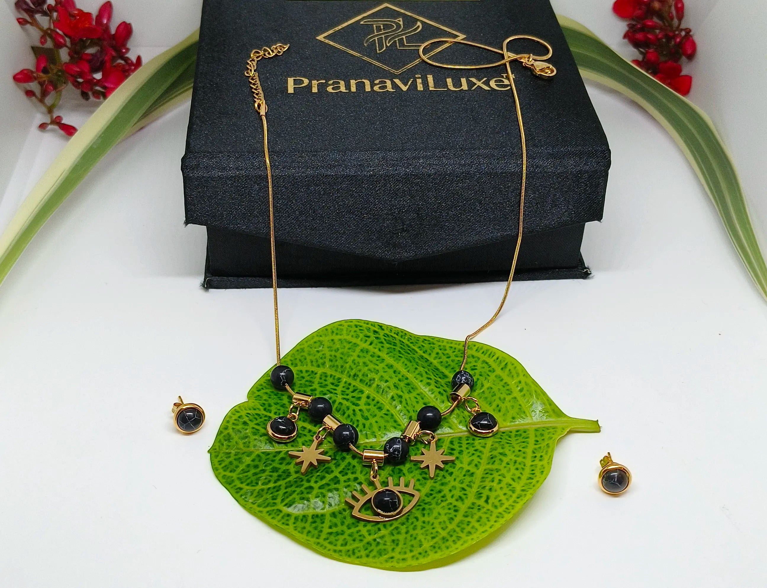 Jewelry set with necklace and earrings on a green leaf, branded 'PranaviLuxe'.