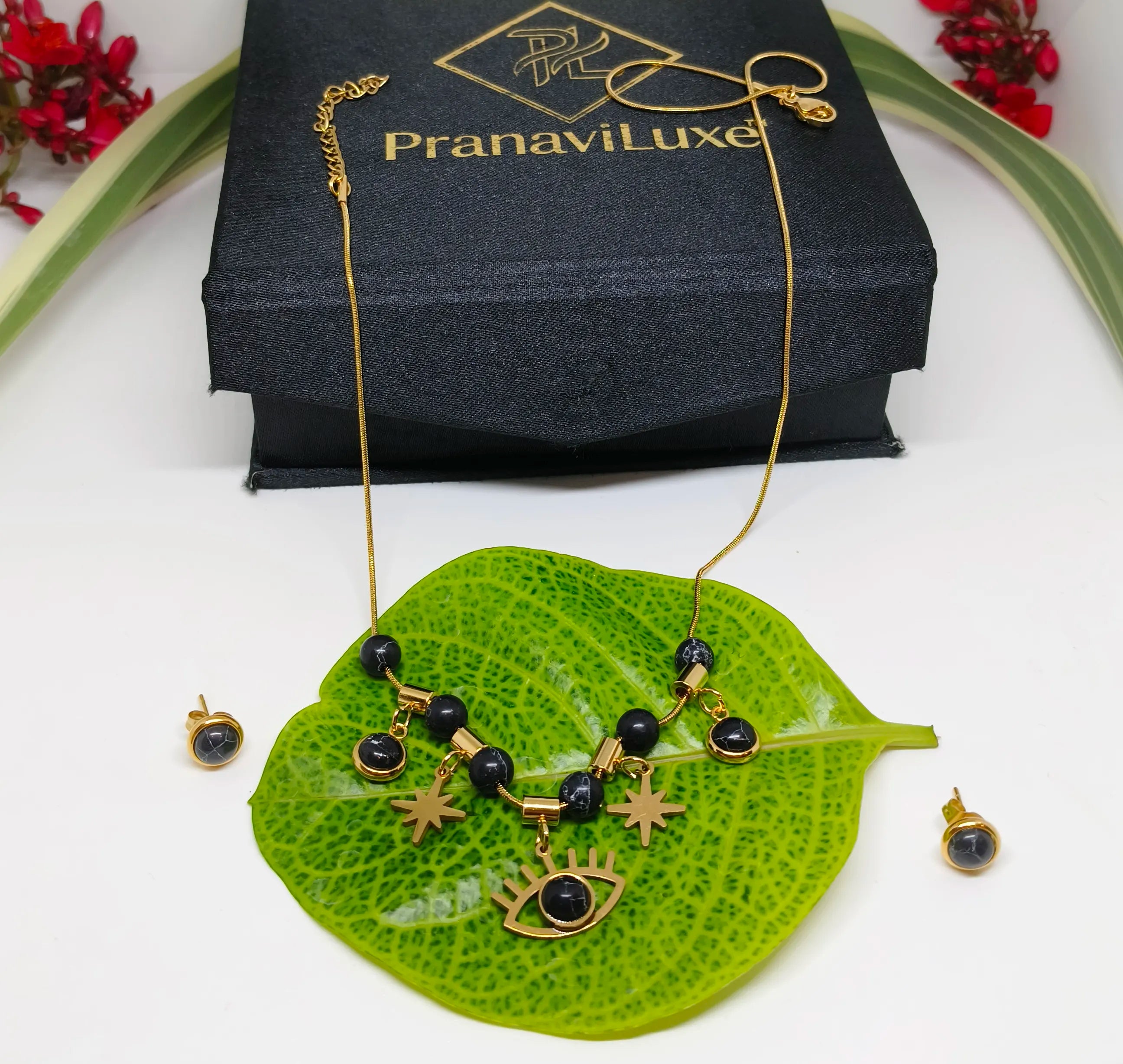 Gold necklace with black beads on a green leaf, PranaviLuxe box in the background