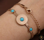 Rose gold bracelet with turquoise stones on a wrist against a dark background
