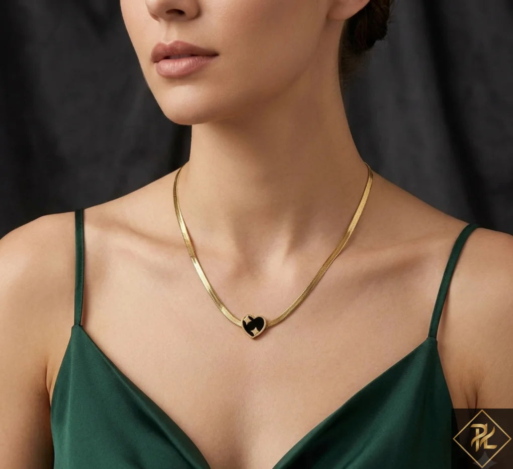 Gold necklace with a heart pendant worn by a person in a green dress against a dark background