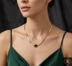 Gold necklace with a heart pendant worn by a person in a green dress against a dark background
