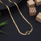 Gold necklace with a heart-shaped pendant on a dark surface with wooden blocks and green leaves.