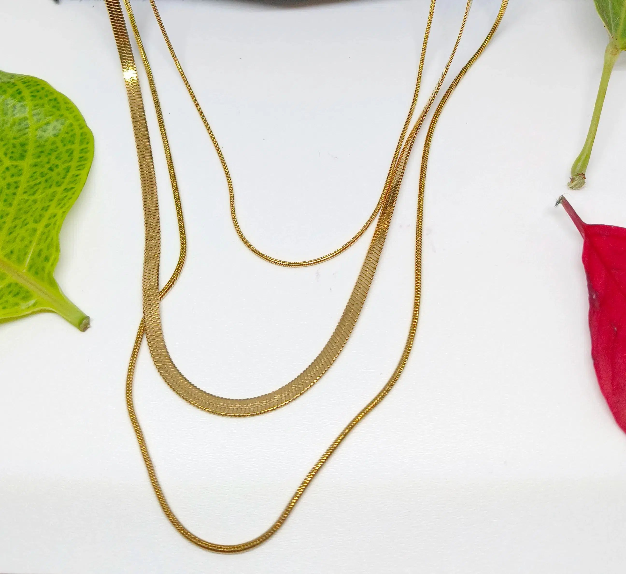 Gold chain necklace on a white surface with leaves