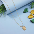 Gold necklace with a rectangular pendant on a light blue background with decorative leaves.
