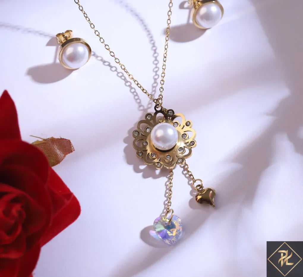 Gold necklace with pearl and crystal pendant on a white background with a red flower.