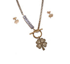 Gold necklace with clover pendant and matching earrings on a white background with a red rose.