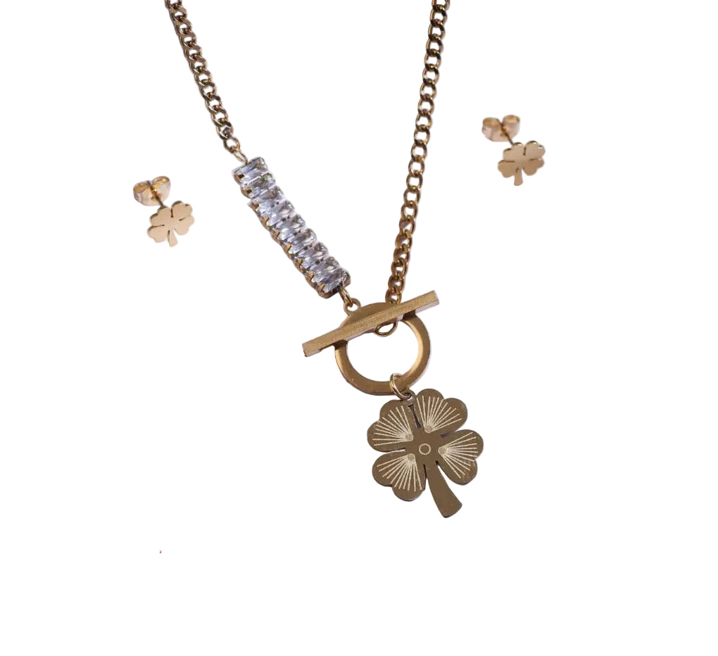 Gold necklace with clover pendant and matching earrings on a white background with a red rose.
