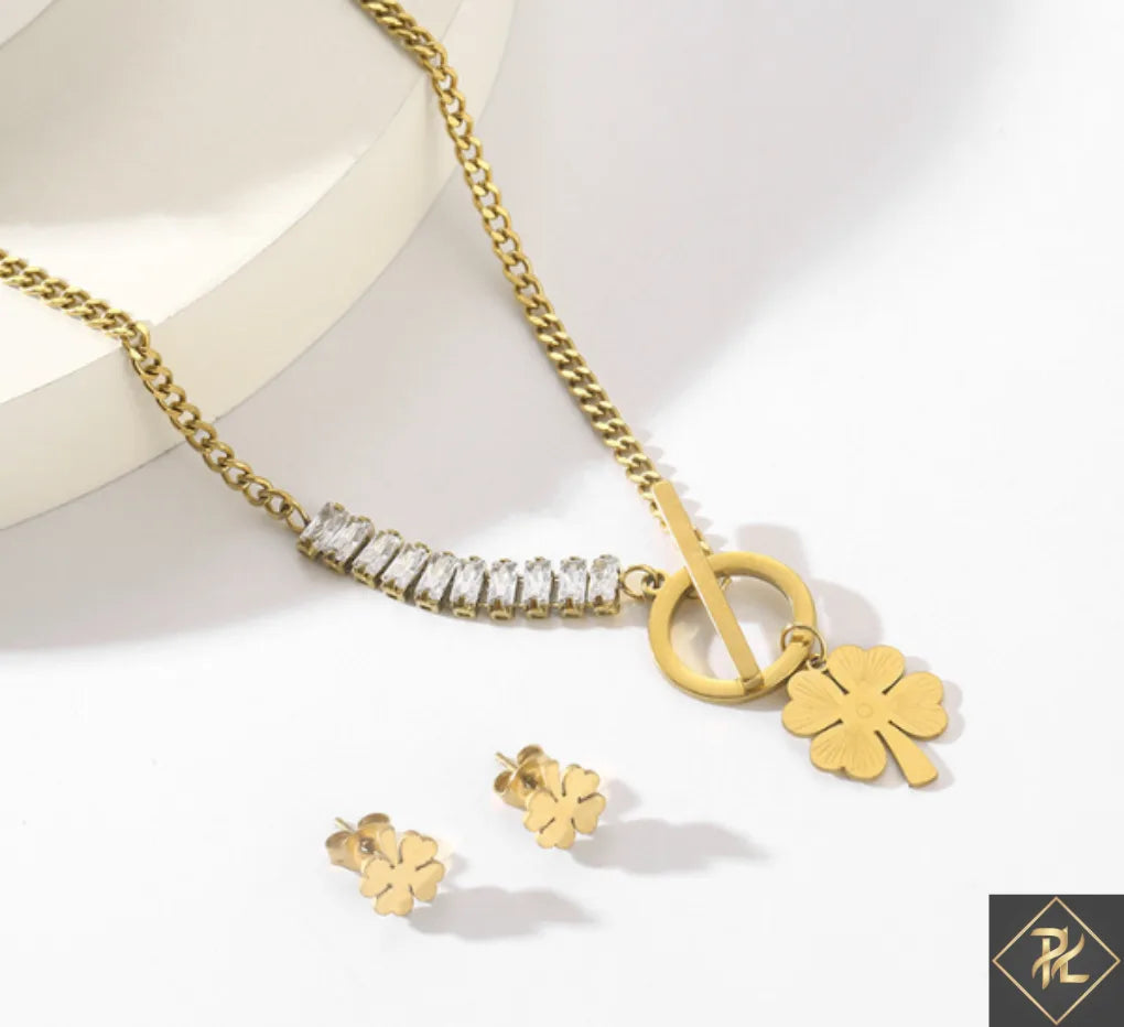 Gold necklace and earrings with a four-leaf clover charm on a white background