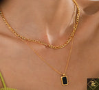 Gold chain necklace with a black pendant on a person's neck
